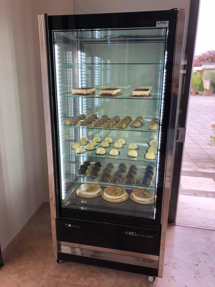 Vetrina in vetro con più ripiani per esporre dolci. Ha una struttura in acciaio inox ed è illuminata internamente.