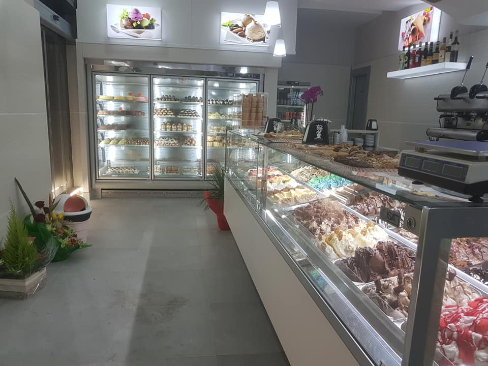 Vista interna di una gelateria con vetrine di dolci e una vetrina refrigerata.