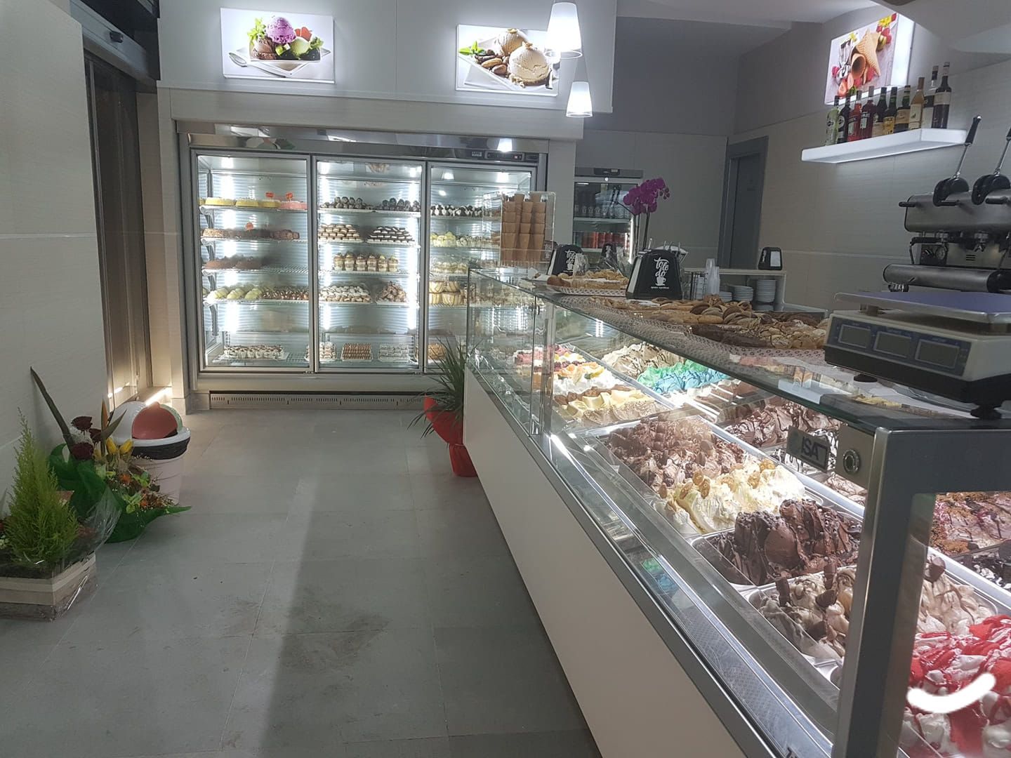 Interno di una gelateria con vetrine in vetro, dessert e illuminazione intensa.