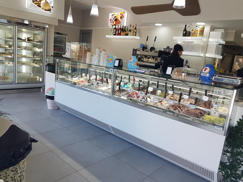 Gelateria con vetrina di gelati, dipendente dietro il bancone.