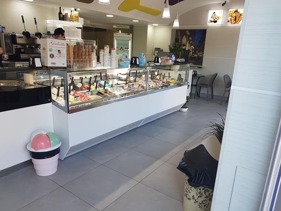 Interno di una gelateria con vetrina per il gelato, bancone e un cliente.