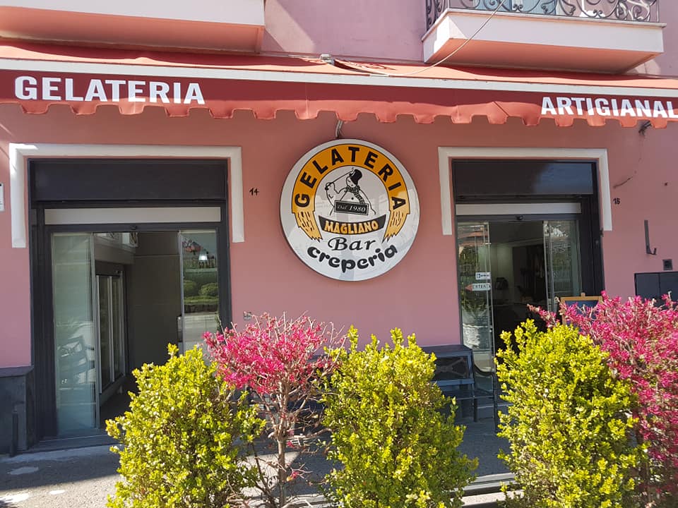 Gelateria con insegna rotonda, tenda da sole e cespugli. C'è scritto