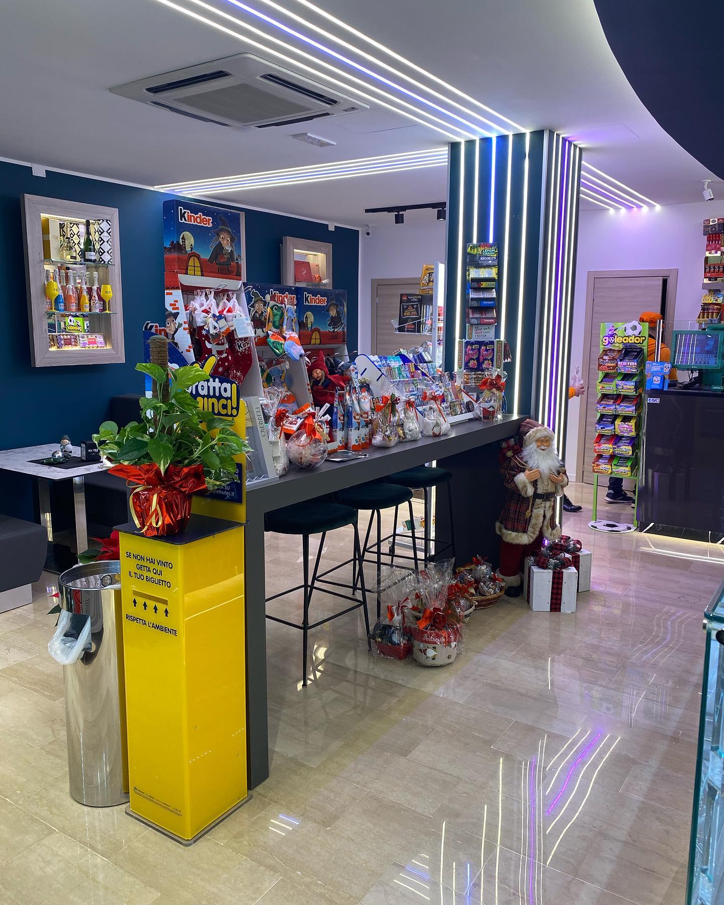 All'interno di un negozio, un bancone con vari prodotti e posti a sedere, decorazioni natalizie e un espositore giallo.