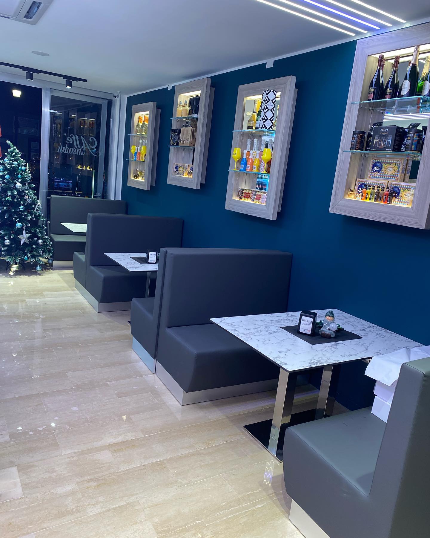 Interno di un piccolo bar con cabine, tavoli, parete blu, vetrine e un albero di Natale.