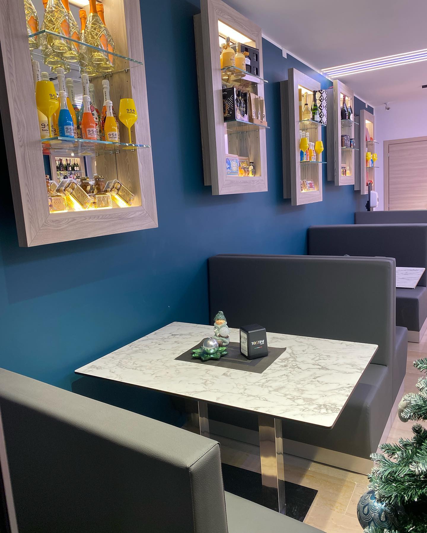 Interno di un ristorante con cabine, tavoli e scaffali che espongono bottiglie su una parete blu.