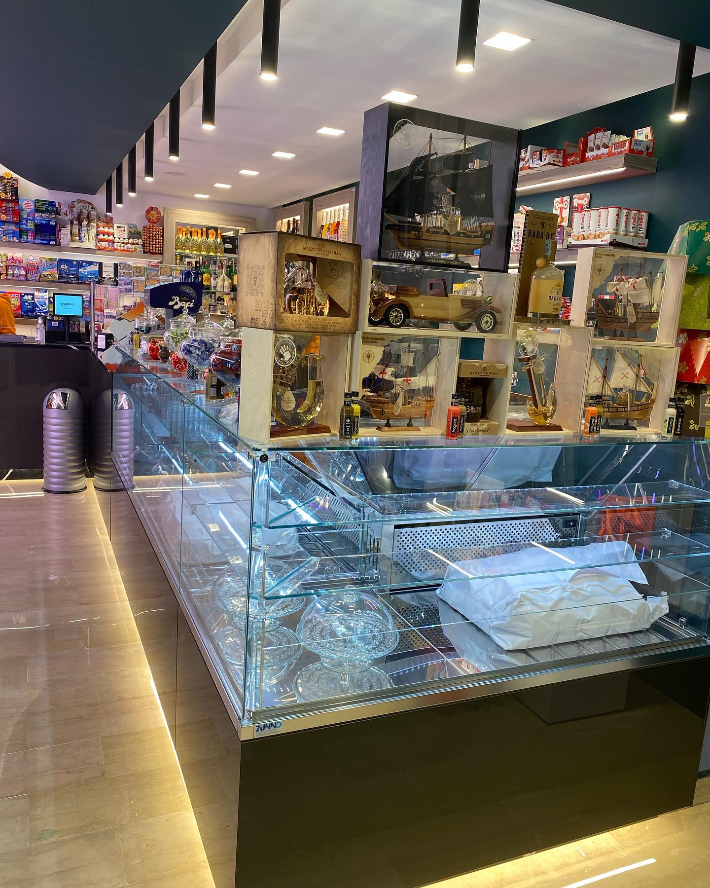 Ripresa dell'interno di un negozio con una vetrina piena di dolciumi e scaffali con vari articoli.