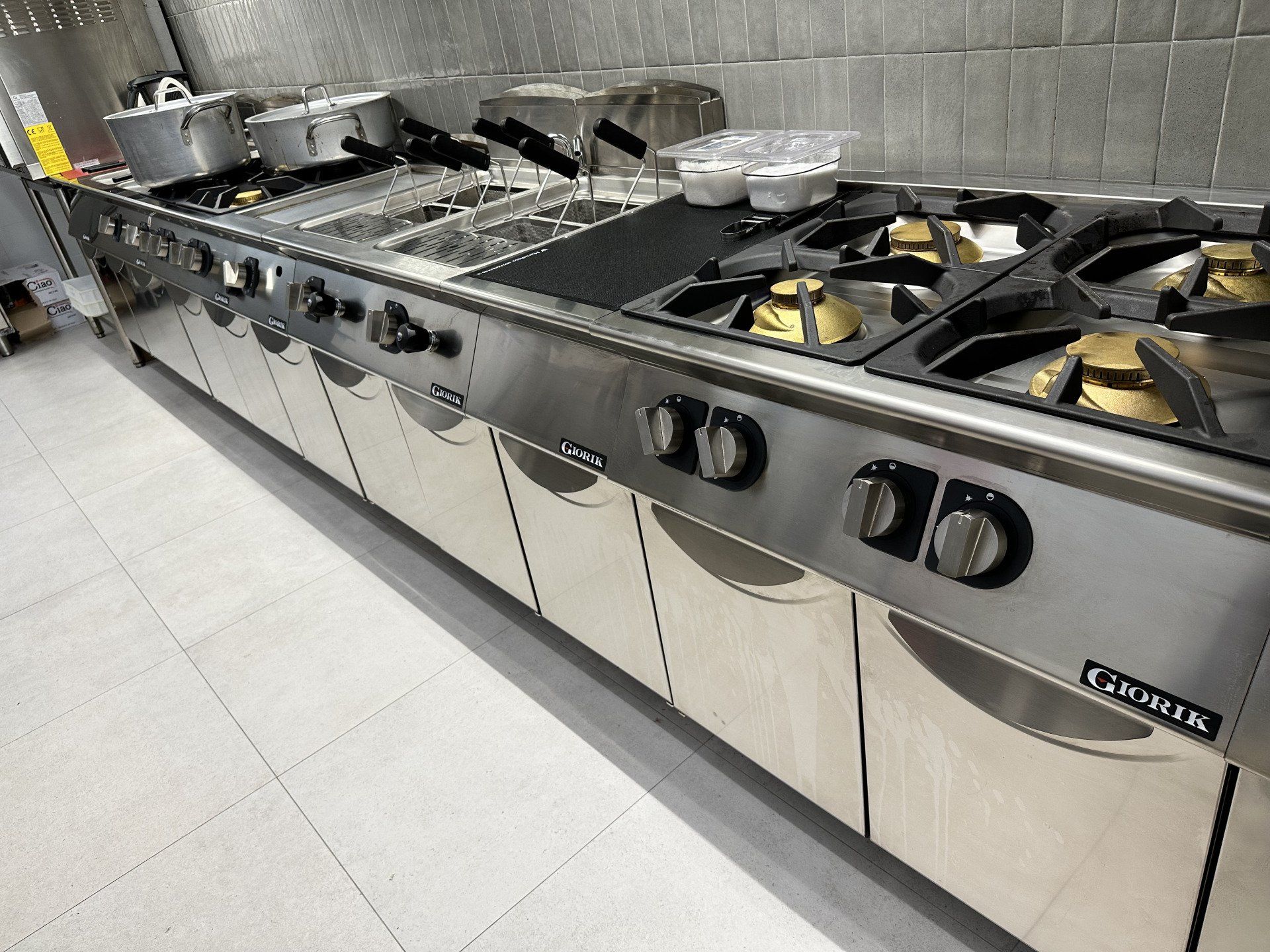 Cucina commerciale in acciaio inox con piani cottura, friggitrici e vani portaoggetti.