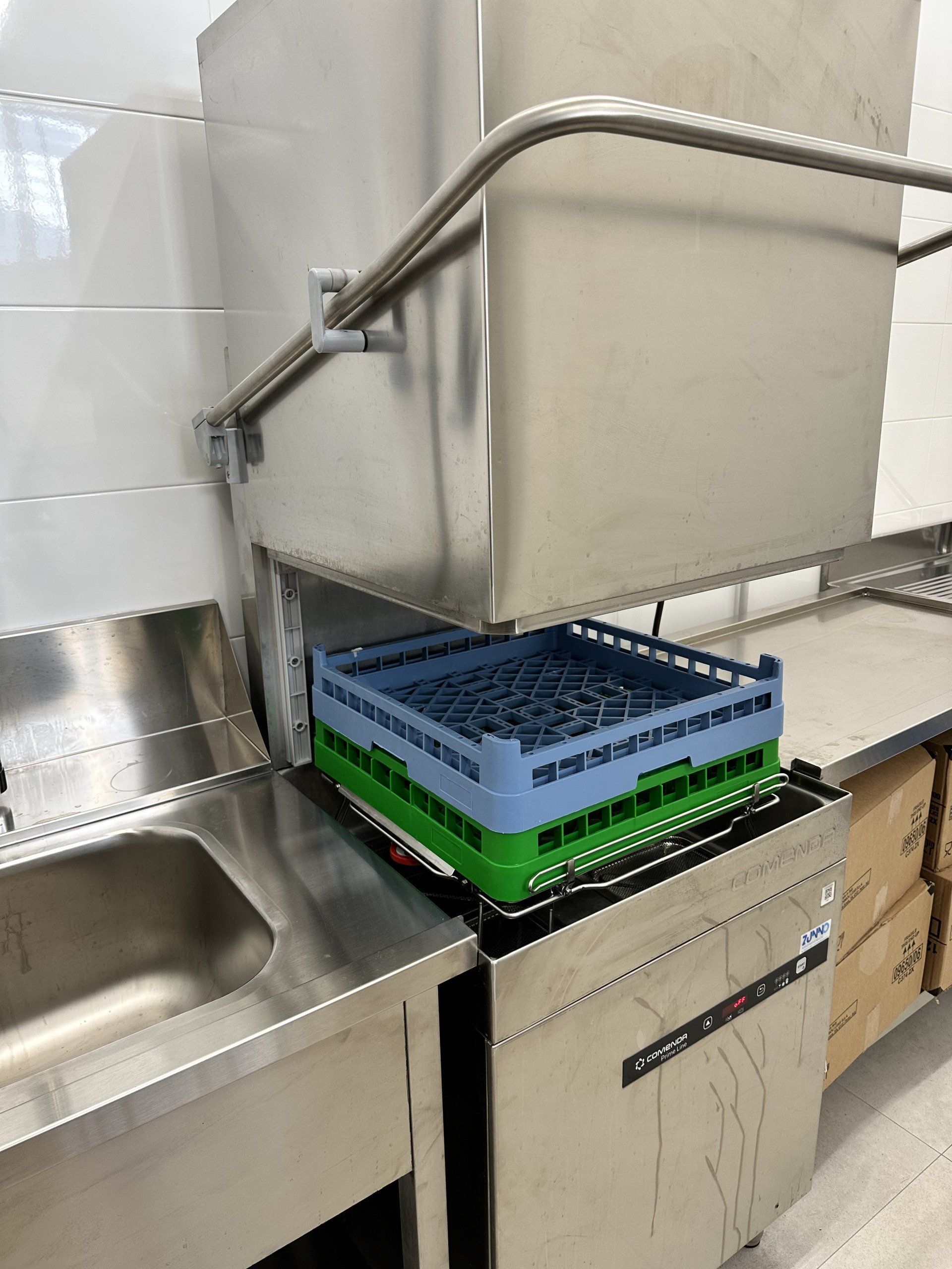 Una lavastoviglie commerciale con cestello per piatti blu e verde in una cucina in acciaio inossidabile.