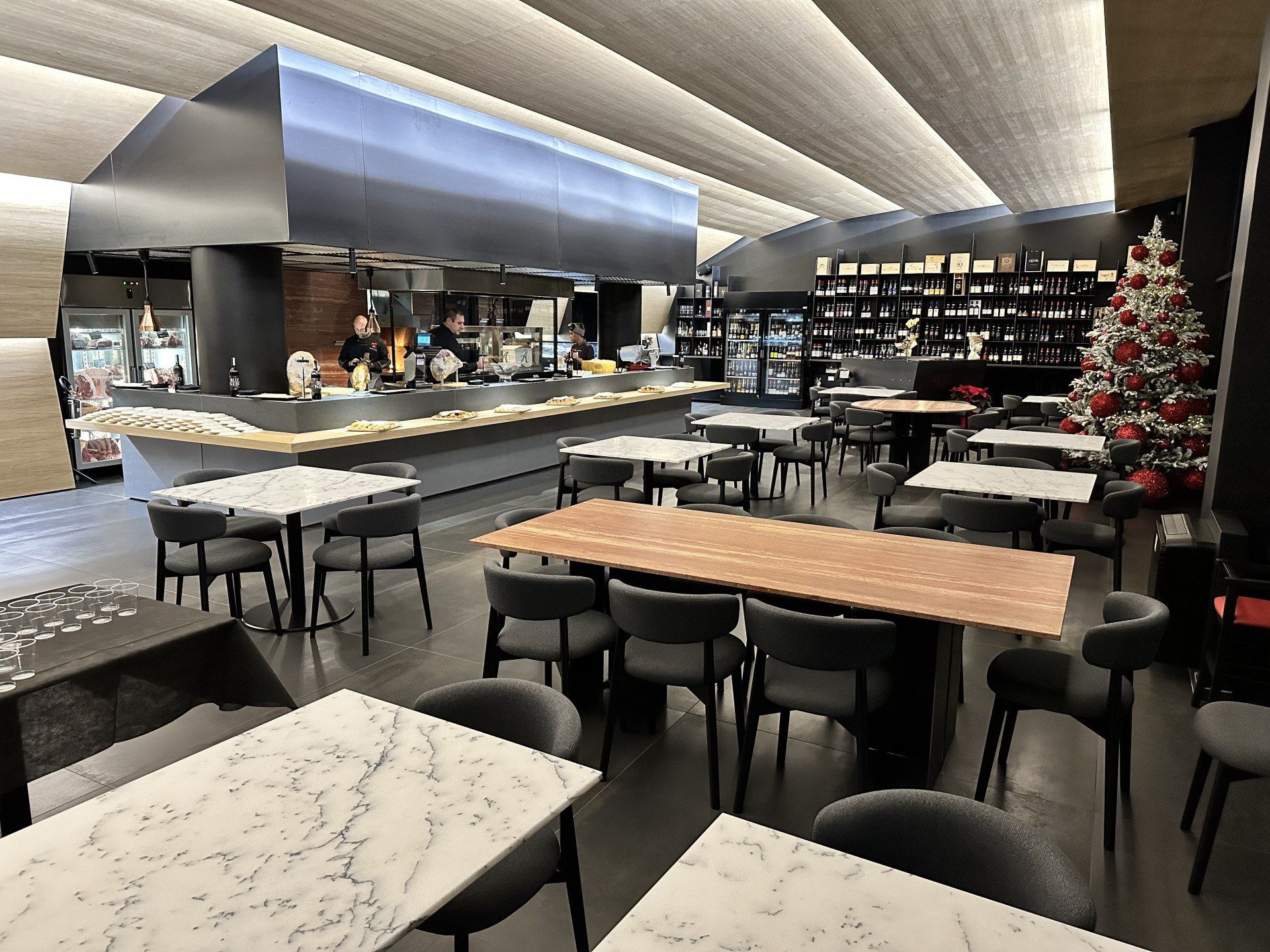 Interno del ristorante con tavoli e sedie, un bar, una zona cucina e un albero di Natale.