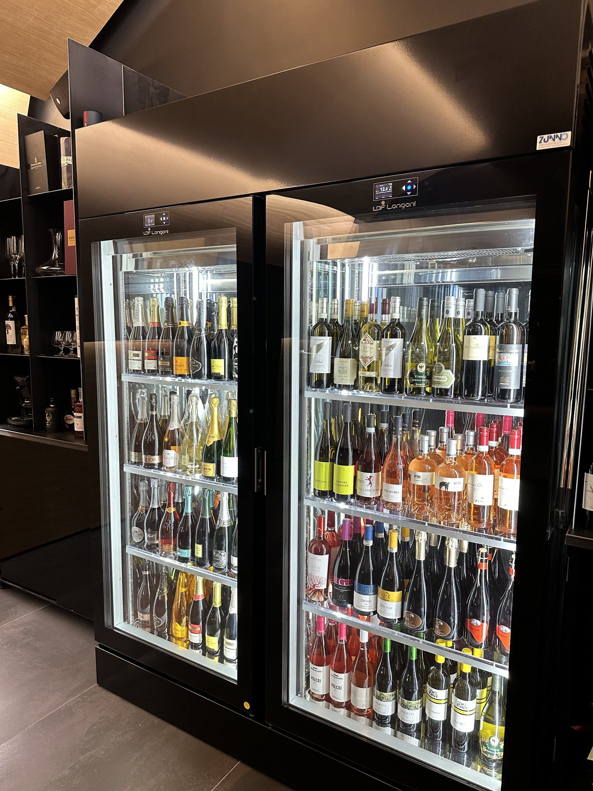 Due frigoriferi neri con sportelli in vetro, pieni di varie bottiglie di vino, illuminati.