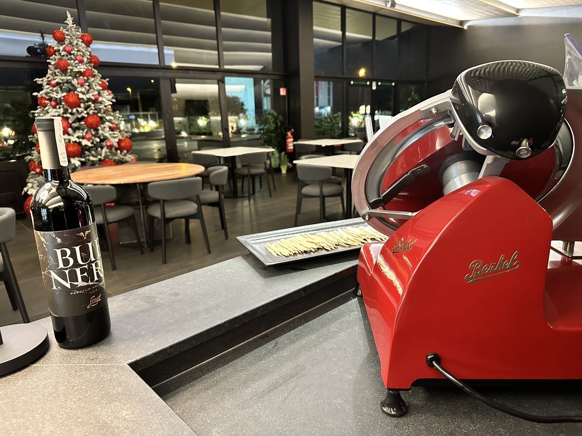 Affettatrice per carne rossa e una bottiglia di vino su un bancone in una sala da pranzo con un albero di Natale.