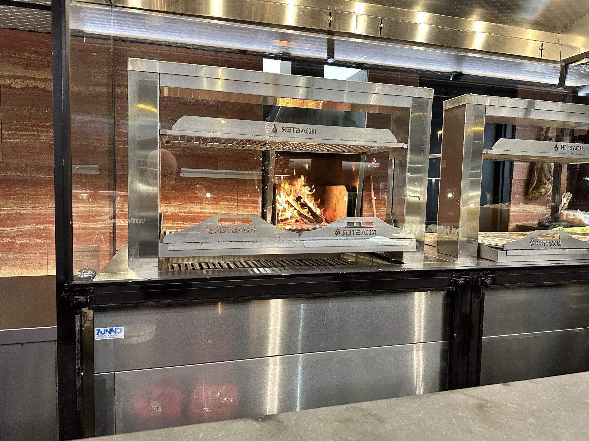 Un girarrosto in acciaio inox con braci ardenti visibili. Ci sono griglie contrassegnate con un testo.