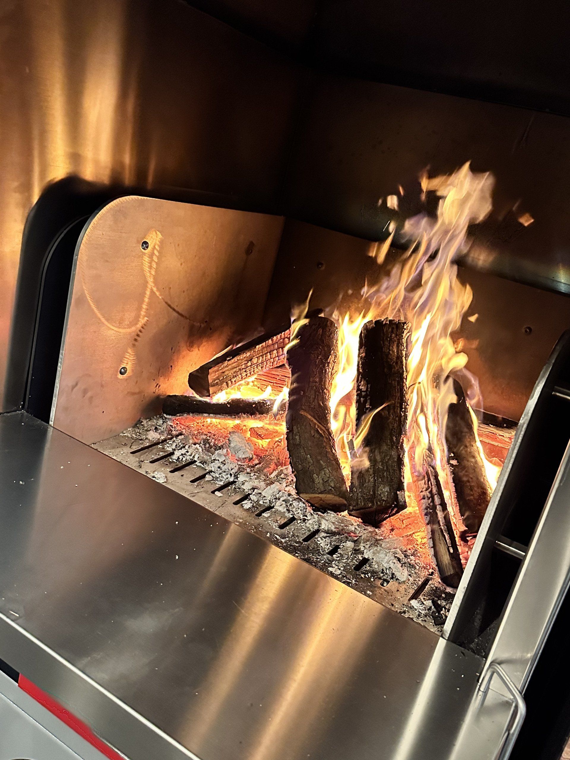 Legna da ardere che arde in un forno in acciaio inossidabile. Fiamme che salgono, braci ardenti.