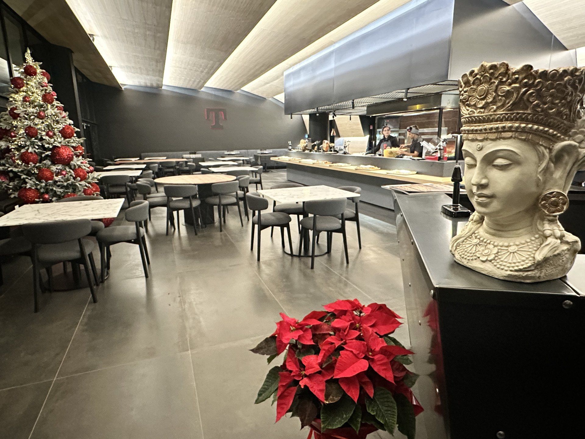 Ristorante interno con tavoli, sedie, albero di Natale e statua a forma di testa di Buddha. Fiori di stella di Natale rossa.