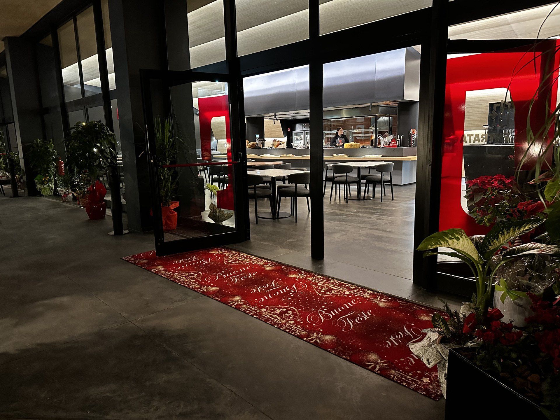 Ingresso al ristorante con tappeto rosso, porte aperte, tavoli e piante.