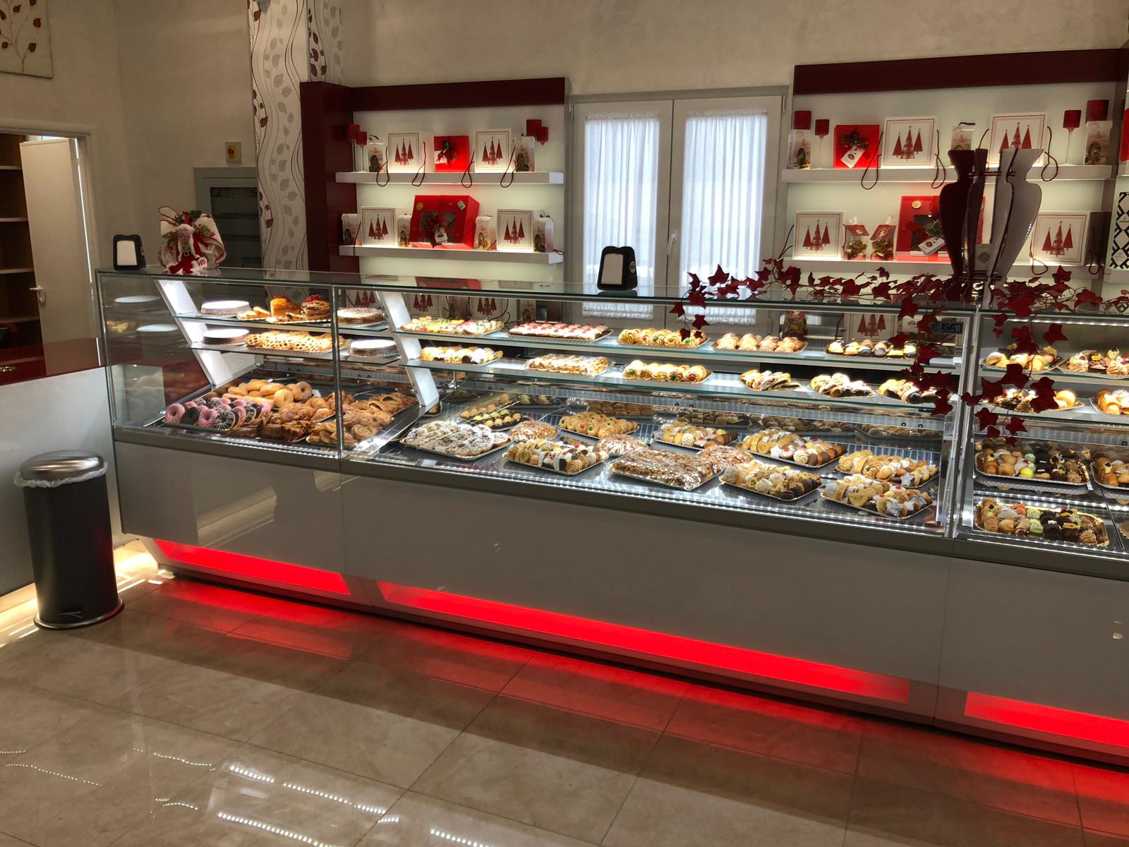 Vetrina di pasticceria in una panetteria, piena di vari dessert, con accenti rossi e luci intense.