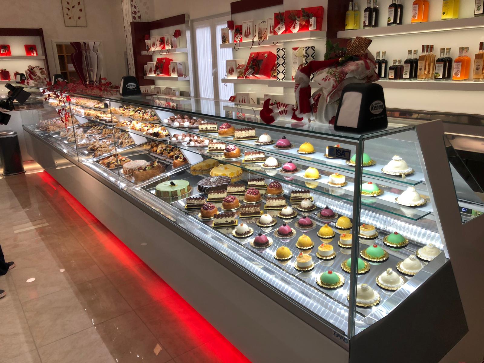 Vetrina di pasticceria piena di torte e dessert in una panetteria ben illuminata.