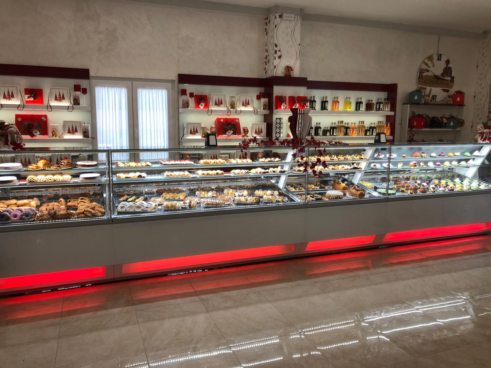 Vetrina di pasticceria in una panetteria con vari dolcetti, illuminazione d'accento rossa e scaffali di prodotti confezionati.