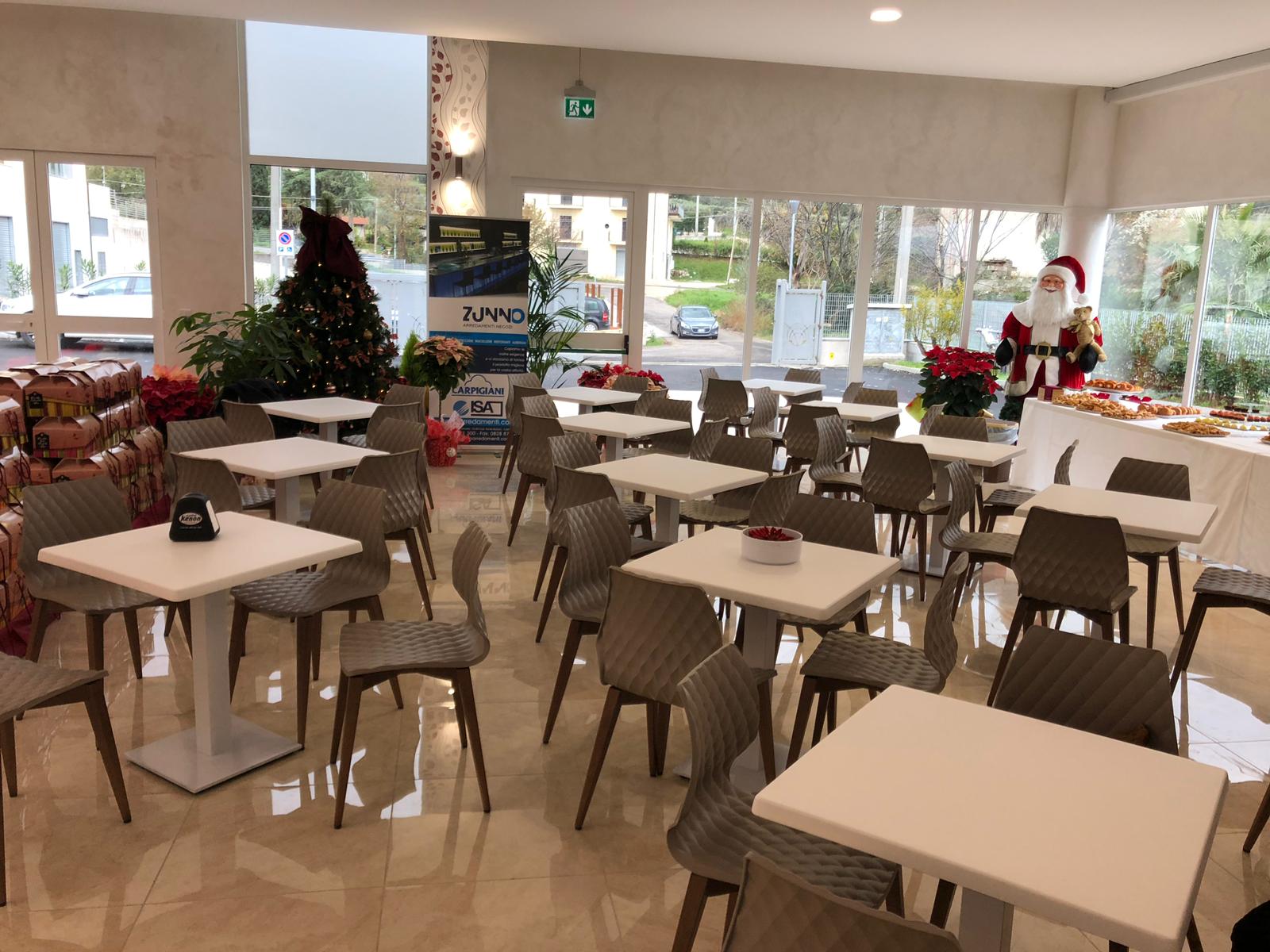 Bar luminoso e spazioso con tavoli quadrati e sedie grigie; decorazioni natalizie.