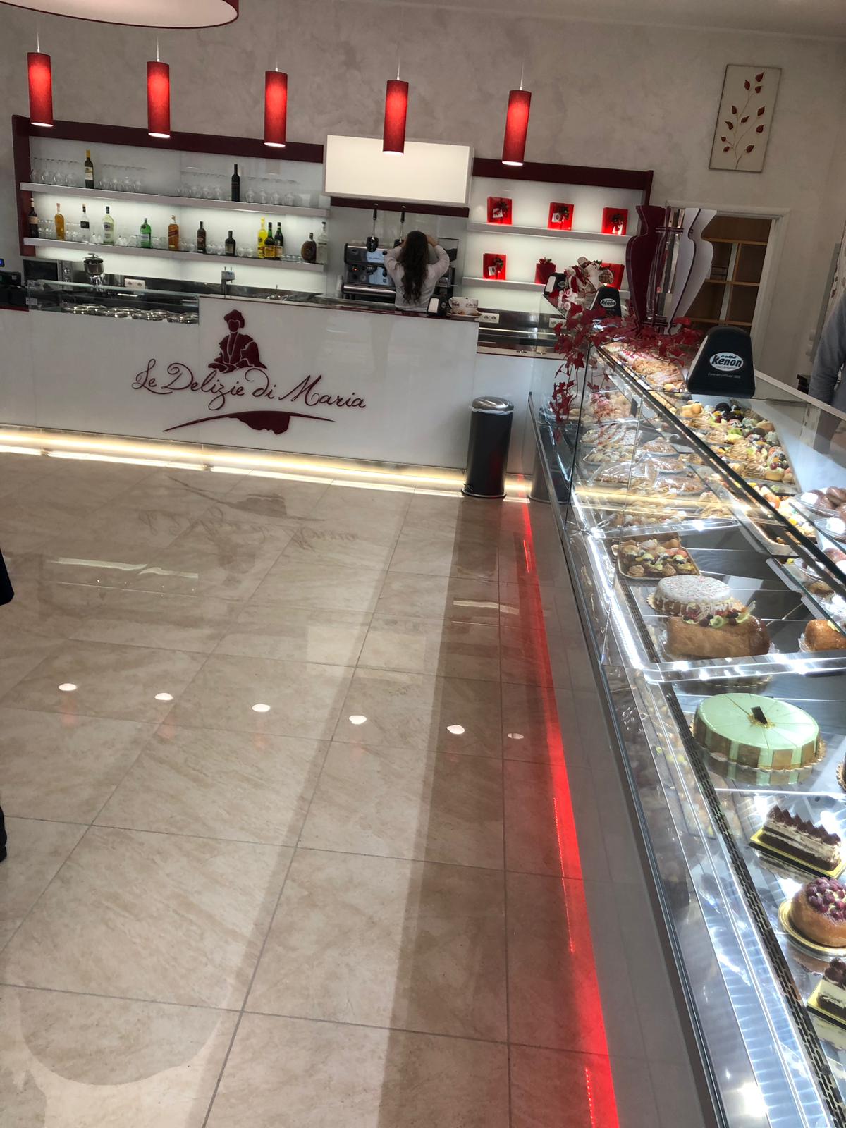 All'interno di una panetteria, una vetrina con torte, dolcetti e un bancone con dettagli rossi.