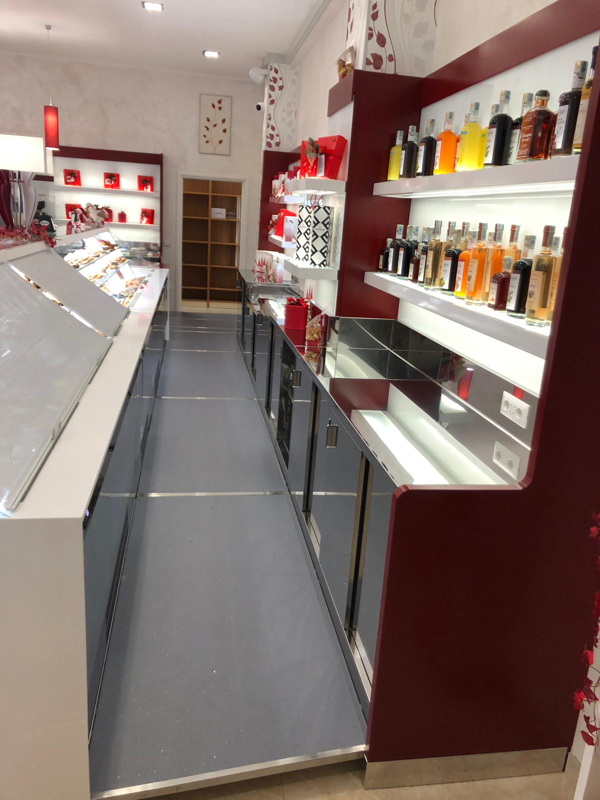 L'interno di un negozio con vetrine, scaffali con prodotti e uno stretto corridoio con una rampa.