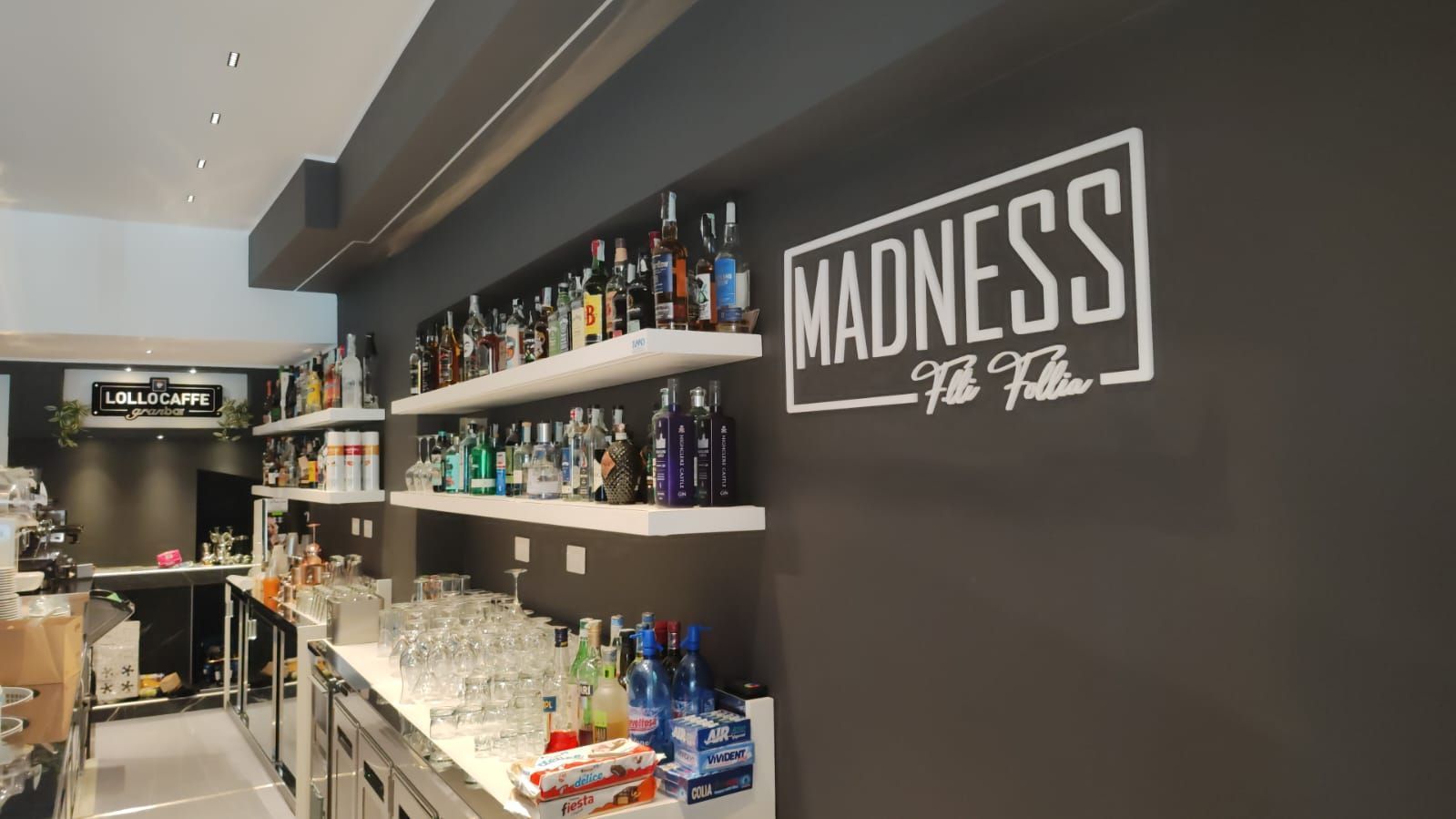 Interno di un bar, con scaffali pieni di bottiglie di liquore e il logo