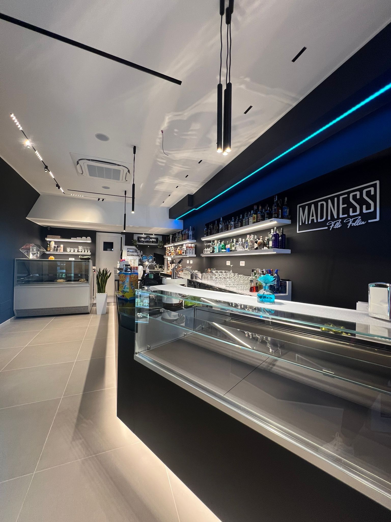 Interno di un bar moderno con dettagli blu e neri, un lungo bancone e l'insegna