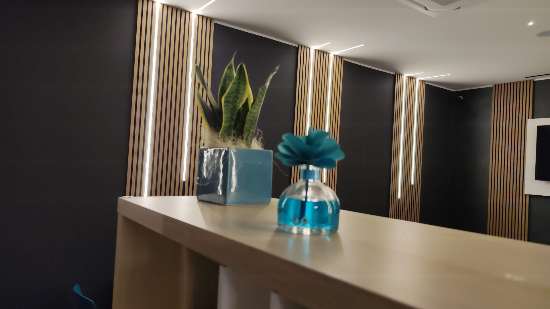 Una moderna area reception per ufficio con bancone dai colori chiari, piante e pannelli decorativi in legno.