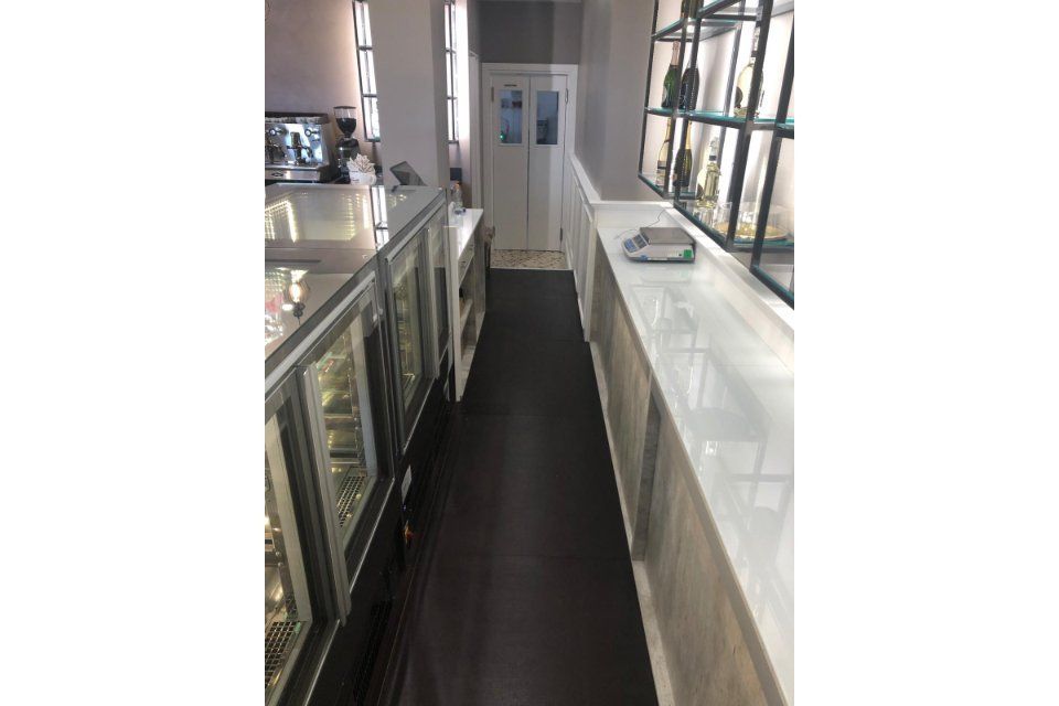 Stretto spazio commerciale con espositori e bancone su entrambi i lati, che conduce a una porta. Pavimento scuro.