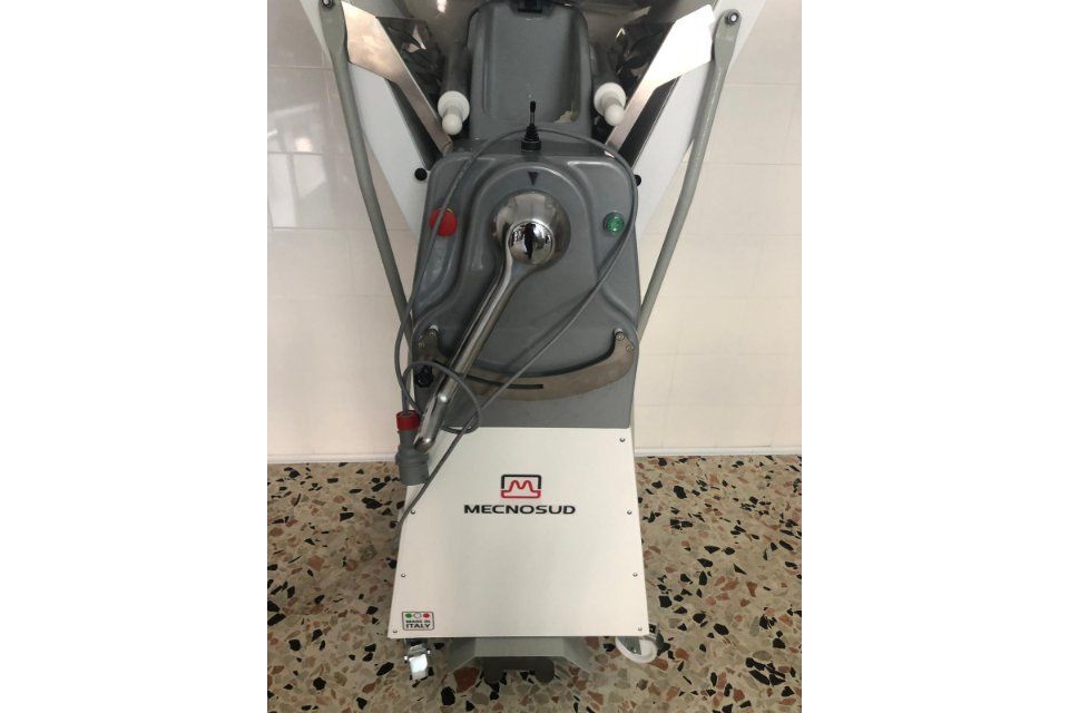 Grande macchina industriale grigia con componenti in acciaio inossidabile, su un pavimento piastrellato. Sulla parte anteriore è stampata la scritta