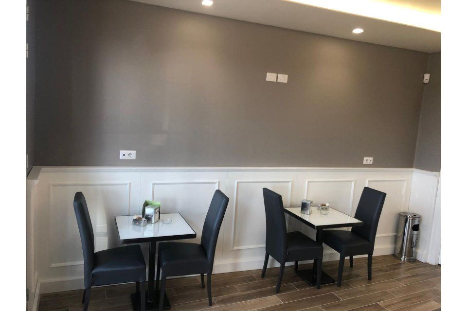 Interno di un bar con tavoli, sedie e pannelli murali grigi.