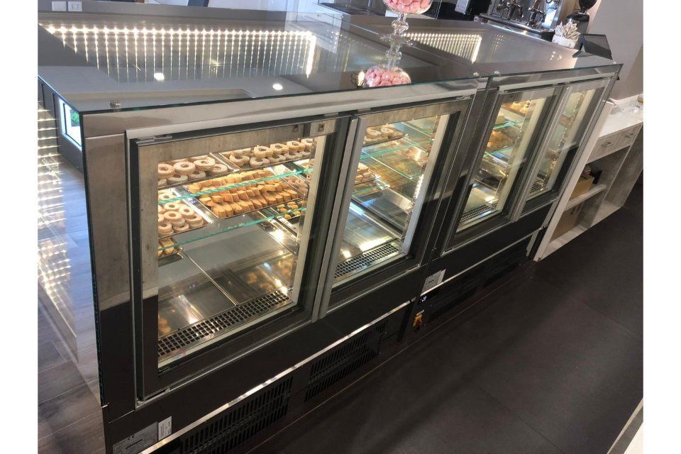 Vetrine piene di ciambelle, interno illuminato, esterno in acciaio inossidabile, allestimento da negozio.