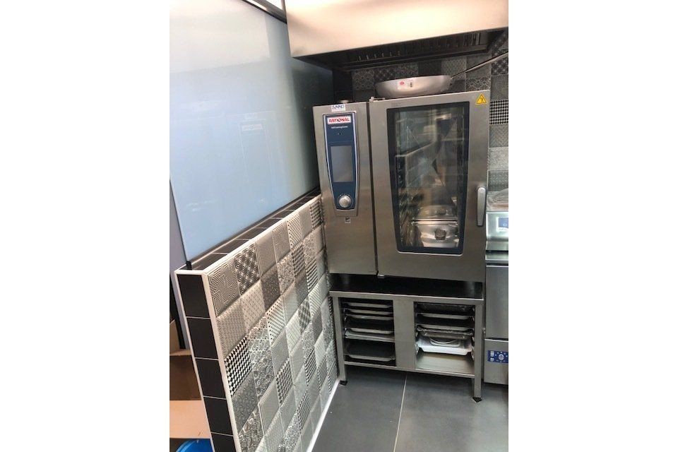 Forno commerciale in un angolo della cucina, con parete piastrellata ed esterno in acciaio inossidabile.