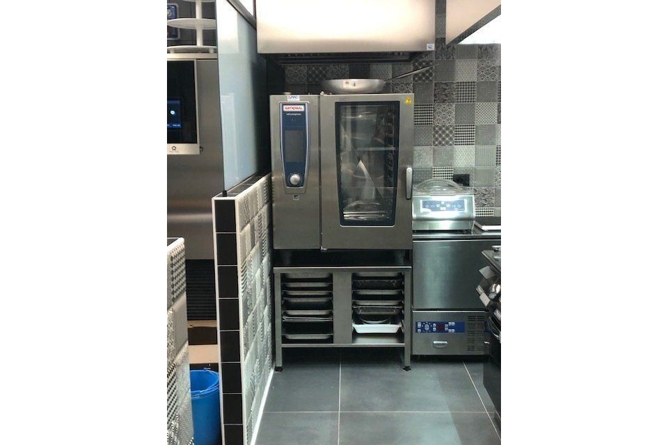 Cucina commerciale con forno, mobiletto di conservazione e macchina per il sottovuoto.