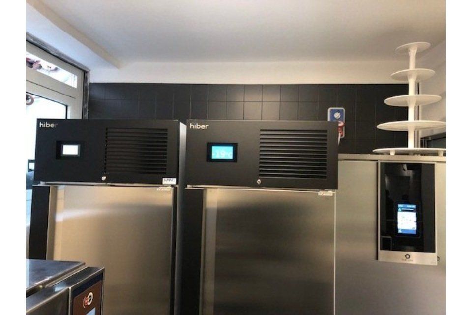 Congelatori neri con pannelli di controllo su frigoriferi in acciaio inossidabile in una cucina commerciale.