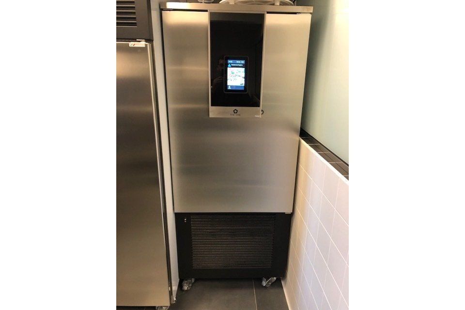 Abbattitore di temperatura commerciale in acciaio inox con pannello di controllo, accanto a un frigorifero.