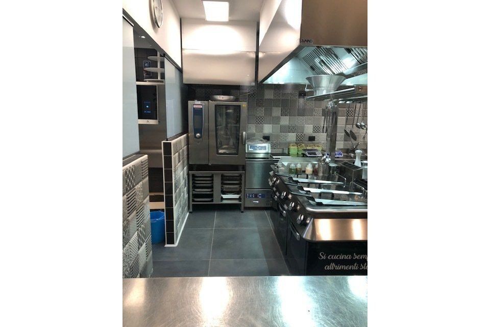Cucina commerciale con elettrodomestici in acciaio inox e cappa di aspirazione.