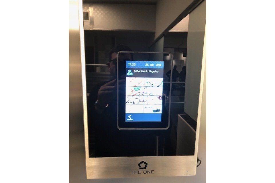 Pannello dell'ascensore con mappa e informazioni. La superficie riflettente mostra una persona che scatta una foto.