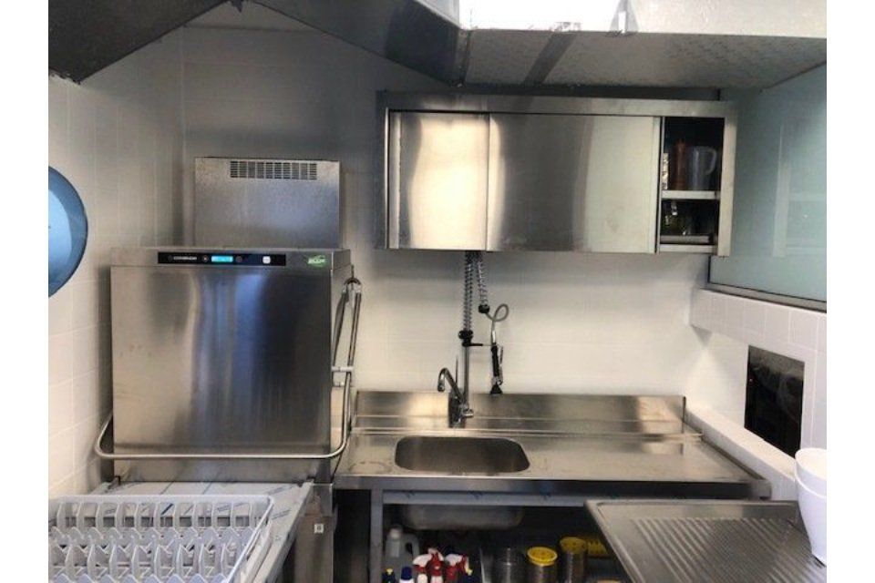 Cucina commerciale in acciaio inox con lavastoviglie, lavello e mobili contenitori.