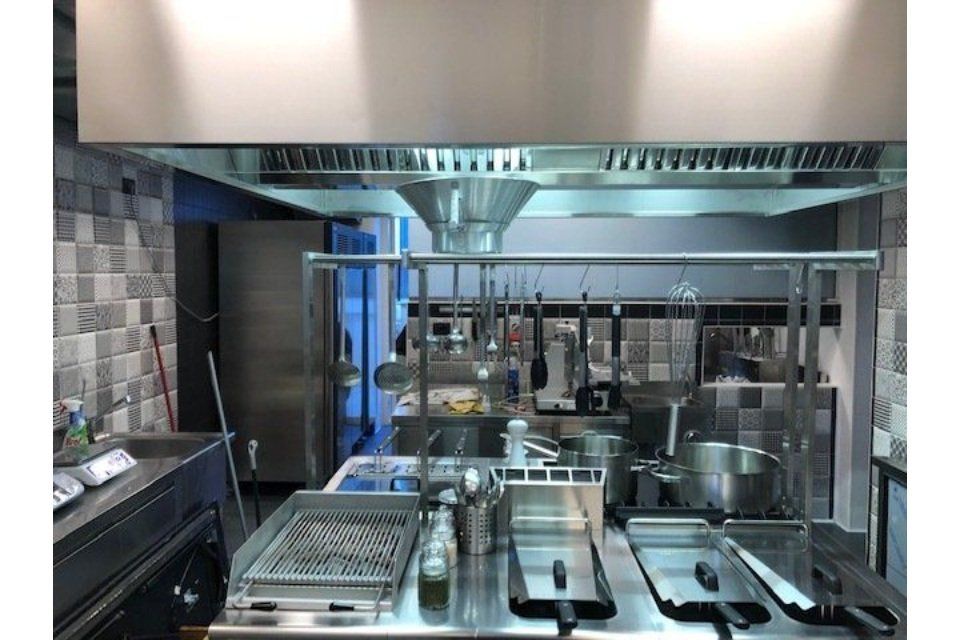 Cucina commerciale con cappa in acciaio inox, attrezzature per cucinare e utensili.