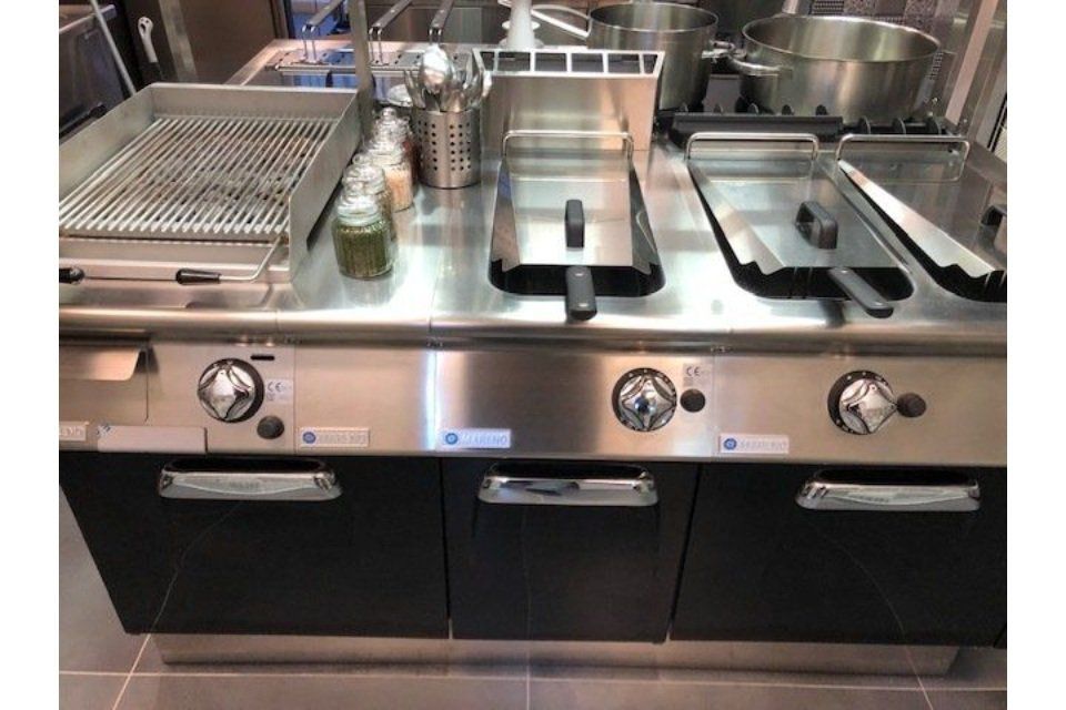 Piano di lavoro per cucina professionale con grill, friggitrice e piano cottura. Acciaio inossidabile, ante nere, manopole.