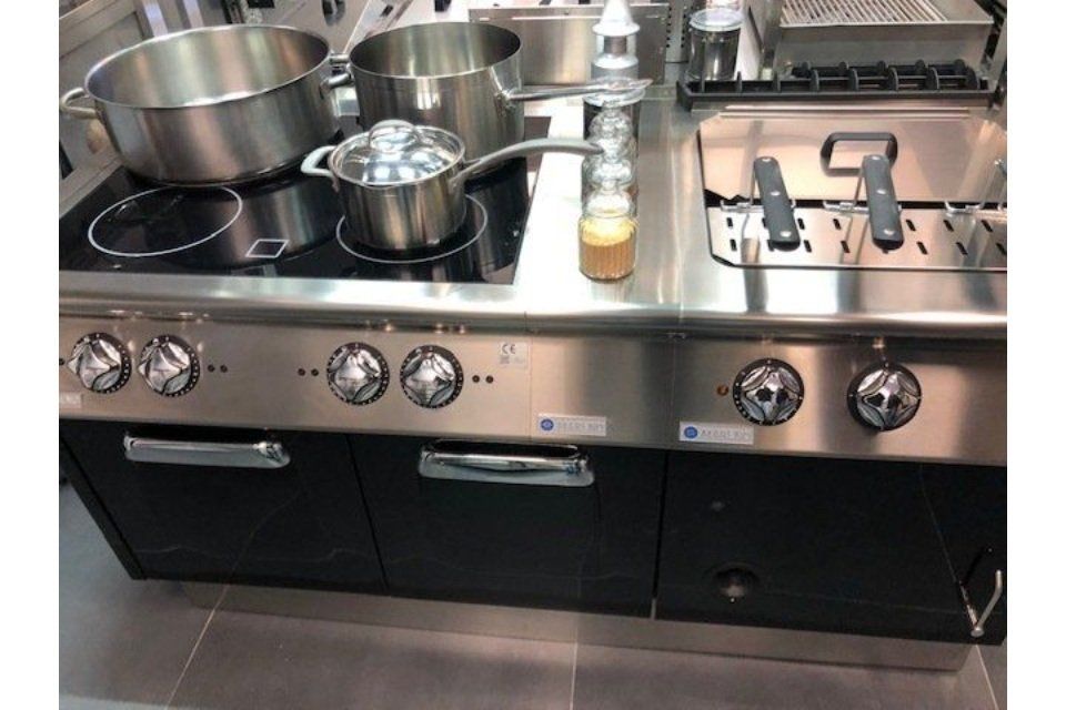 Cucina commerciale in acciaio inox con pentole, padelle, piano cottura, friggitrice e forno.
