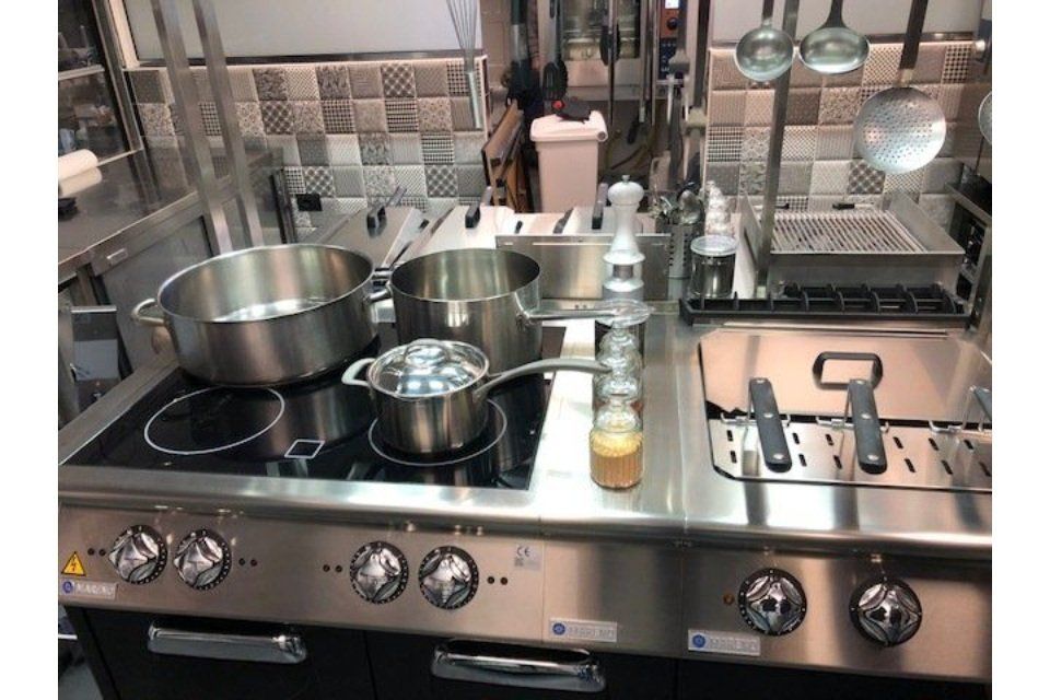 Cucina commerciale in acciaio inox con pentole, padelle e utensili.