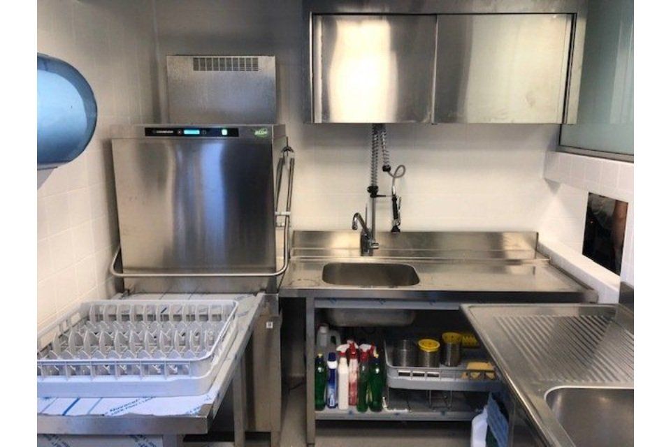Cucina commerciale in acciaio inox con lavastoviglie, lavello e spazio di stoccaggio.