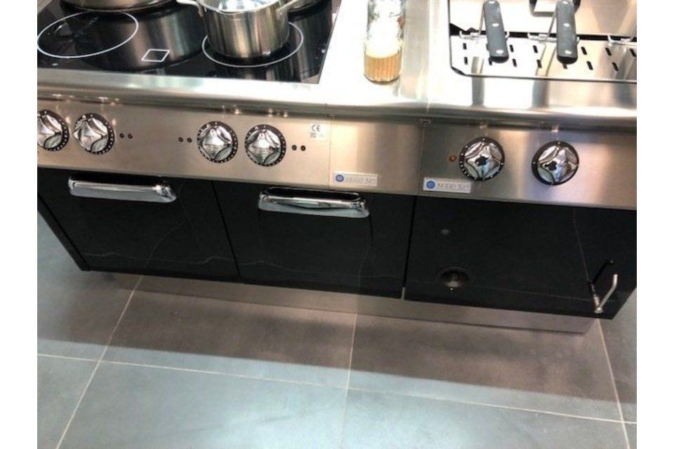 Cucina in acciaio inox e nero con piano cottura, forni e manopole di controllo.