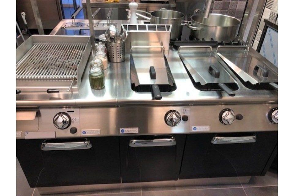 Attrezzature per la cottura in acciaio inossidabile per cucine commerciali, tra cui grill, friggitrici e fornelli.