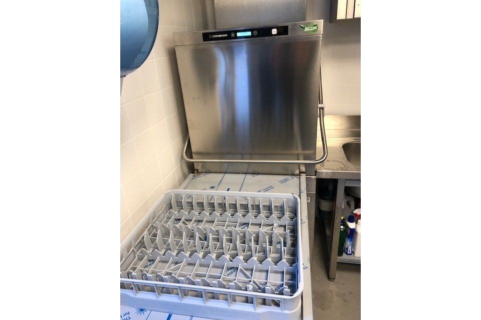 Una lavastoviglie commerciale con lo sportello aperto e il cestello dei bicchieri visibile, in una cucina.