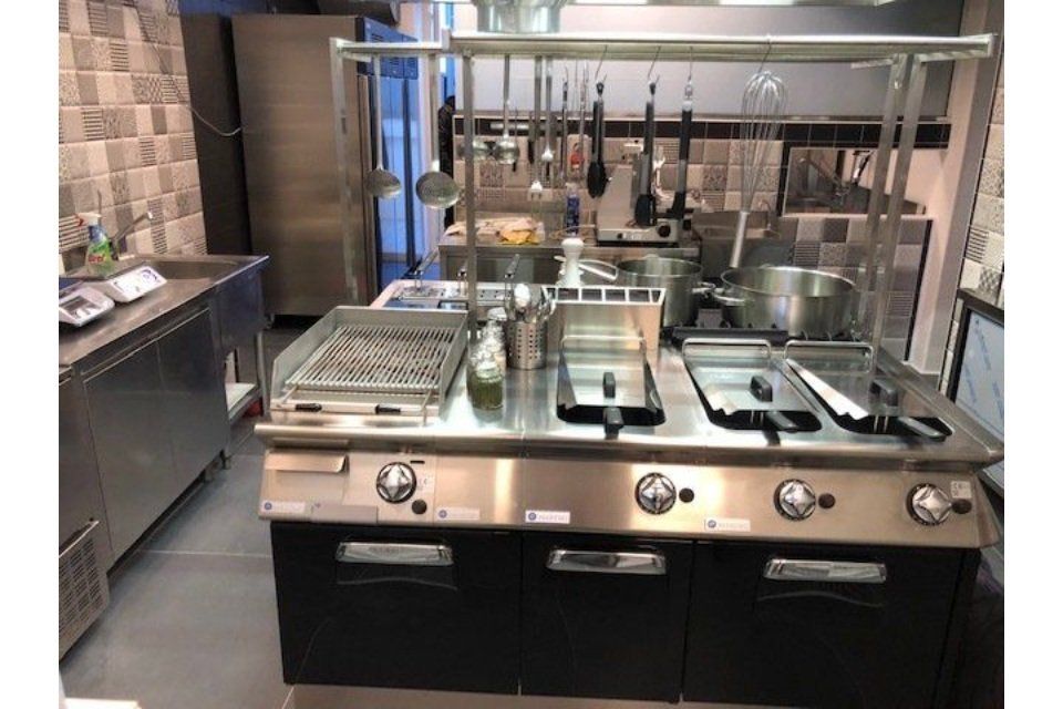 Cucina commerciale con elettrodomestici in acciaio inossidabile, tra cui grill, friggitrici e pentole.