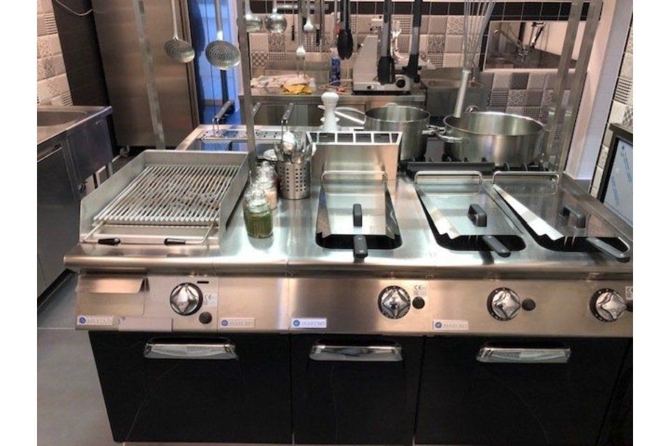 Isola di cottura per cucina commerciale con grill, friggitrici e pentole.