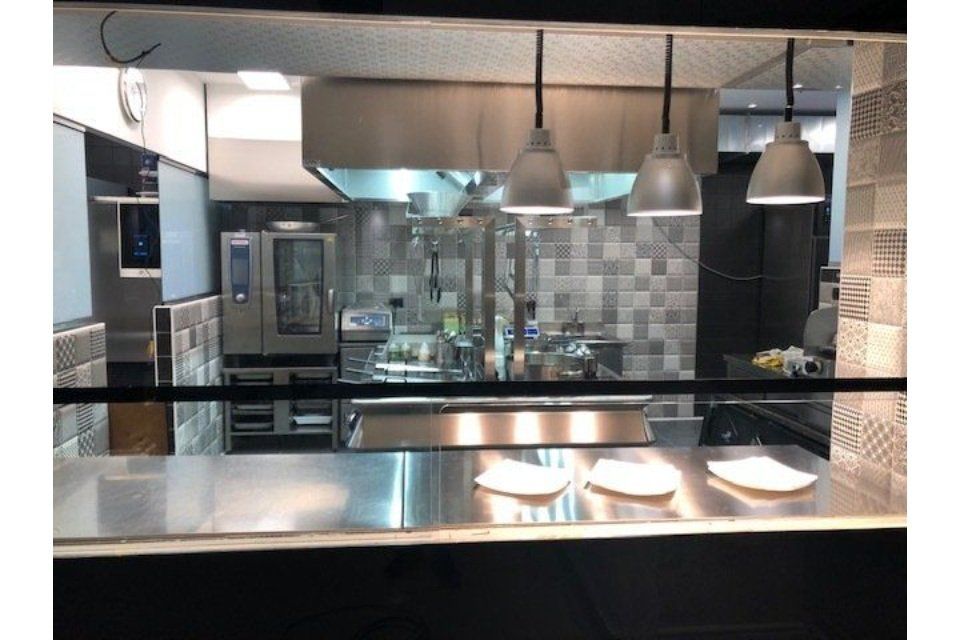 Cucina del ristorante con bancone in acciaio inox, attrezzatura da cucina e luci sospese.